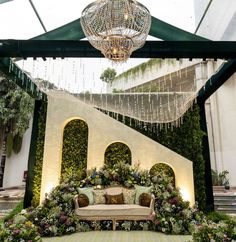 a couch sitting under a chandelier in a room filled with plants and flowers