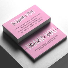 two pink business cards with the words thank you written on them, sitting on top of each other