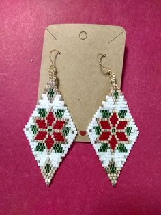 a pair of beaded earrings with poinsettis on them sitting in front of a card