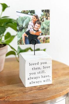 a wooden block with a photo on it sitting on top of a table next to a potted plant