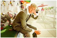 a man in a suit and tie sitting on a bench with stuffed animals behind him