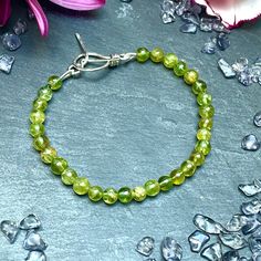 Gorgeous green Peridot bracelet with a hand crafted sterling silver toggle clasp. The bracelet measures 7.5 inches in length, the standard measurement for a bracelet. It has been strung on green coloured silk thread. It's a versitile bracelet which can be worn in the day or the evening. Peridot, in shades of olive, is one of the few gemstones that forms in only one colour. It carries the gift of inner radiance, sharpening the mind and opening it to new levels of awareness and growth.  Peridot is Green Faceted Round Bead Bracelets, Green Faceted Bracelets, Green Bangle Crystal Bracelet With Natural Stones, Green Natural Stones Crystal Bangle Bracelet, Adjustable Peridot Bracelets For Gifts, Green Faceted Bead Bangle Jewelry, Green Faceted Beads Bangle Bracelet, Green Faceted Beads Bangle, Green Faceted Bracelets For Gift