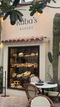 the outside of a bakery with tables and chairs in front of it, surrounded by cacti