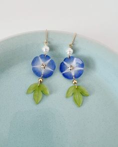 a pair of blue and green flower earrings on a plate