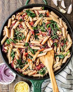 a pan filled with pasta and spinach on top of a table next to garlic