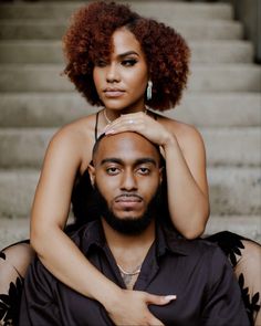 a man and woman sitting next to each other in front of some stairs with their arms around one another