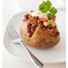 a white plate topped with a baked potato covered in beans and veggies next to a fork