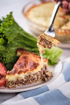 a slice of quiche being lifted with a fork from a white plate on a blue and white table cloth