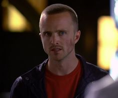 a man in a red shirt and black jacket looking at another man with blue eyes