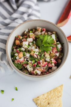 a white bowl filled with chopped vegetables and cilantro next to tortilla chips