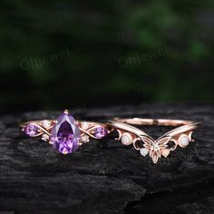 two gold rings with amethysts and pearls on them sitting on a rock