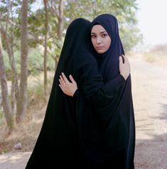 a woman in a black hijab is hugging her head with both hands on her chest