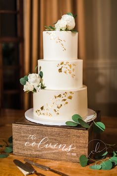 a wedding cake with white flowers and greenery sits on top of a wooden box