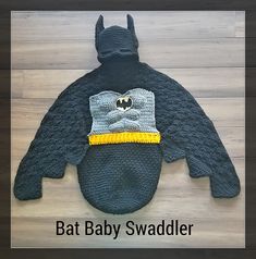 a knitted bat baby sweater with a batman hat on it's head and the words bat baby swadler written below