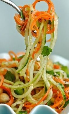 a fork is lifting some food out of a white bowl with green beans and carrots