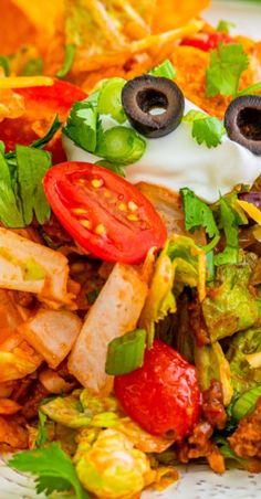 a salad with tomatoes, lettuce and olives on it is topped with sour cream