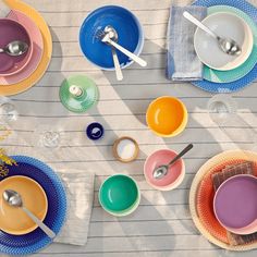 colorful plates and bowls on a table with utensils, spoons and napkins