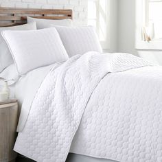 a bed with white bedspread and pillows in front of a brick wall next to a window