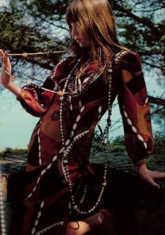 a woman with long hair sitting on the ground in a dress and holding a stick