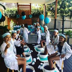 a group of women sitting on top of buckets in front of a table filled with blue balloons