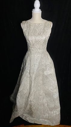 "Fabulous 1960's metallic silver and white Emma Domb formal dress with low back and high neckline. Zipper up the back and tulle under the skirt to help keep it full. Skirt near the hem has an orange spot about the size of a quarter Women's small/medium 36\" bust 27\" waist Open hips 60\" shoulder to hem" Fitted Full Skirt Evening Wedding Dress, White A-line Fitted Mother Of The Bride Dress, Fitted Gown With Full Skirt For Party, White A-line Vintage Dress For Party, Silver Ball Gown Evening Dress With Fitted Bodice, Elegant Vintage Dress With Full Skirt For Party, Vintage A-line Wedding Evening Dress, Vintage Silver Dress For Formal Occasions, Silver Vintage Dress For Formal Occasions