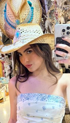 a woman in a white dress and hat taking a selfie with her cell phone