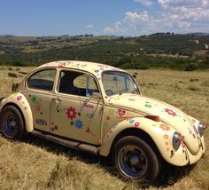 an old vw bug painted with flowers on the side in a grassy field,