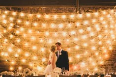 a bride and groom standing next to each other in front of a wall covered with lights