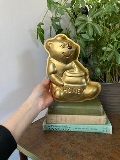 a gold bear statue sitting on top of a book next to a potted plant