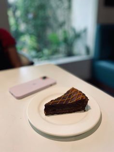 a piece of chocolate cake sitting on top of a white plate next to a cell phone