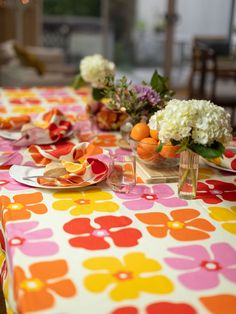 the table is set with flowers and plates on it, along with other dishes that include oranges and white hydrangeas