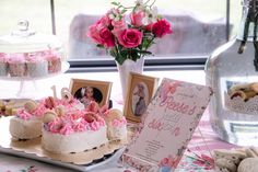 a table topped with cakes covered in frosting and pink icing next to a vase filled with flowers