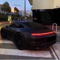 a black sports car parked in front of a parking lot at night with its lights on