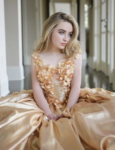 a woman sitting on top of a bed in a golden dress with ruffles