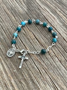 "Beautifully Handmade Rosary bracelet! Beads are 6mm polished (Topaz Blue) Apatite semi-precious stone, Cross is a 7/8\" silver St. Benedict crucifix, and mini medal is a 1/2\" mini medal with amazing details **Mini Medal Choices**  1.  Blue Miraculous Mary  2. Miraculous Mary  3. Holy Spirit  4. 5 Way Cross  5. Holy Family / Holy Spirit  6. Guardian Angel / St. Michael Each one of my rosary bracelets starts its life as a spool of wire and a handful of beads. It is carefully assembled one link at a time so no two are ever exactly alike. A truly one-of-a-kind gift for your one-of-a-kind someone! They are sturdy enough to withstand the test of time, and sentimental enough to pass down for generations to come! **Size options**   1.  5 1/2\" Baby-age 3   2.  6\" - age 4-7   3.  6 1/2\" - age 8 Handmade Rosary, Stone Cross, Decade Rosary, St Benedict, Catholic Rosary, Rosary Bracelet, Birthstone Bracelet, Rosary Catholic, Birthstone Gifts