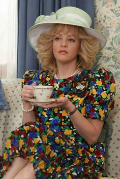 a woman sitting on top of a couch holding a cup and saucer in her hands