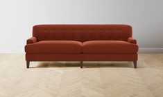 an orange couch sitting on top of a hard wood floor next to a white wall