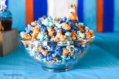 a bowl filled with blue and orange popcorn on top of a table next to cupcakes