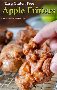 a hand picking up an apple fritter from a cooling rack with apples in the background