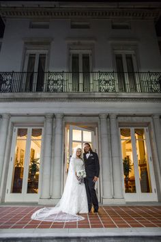 a bride and groom standing in front of a large white building at night with the lights on