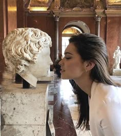 a woman is kissing a bust of a man in a room with marble sculptures on the walls