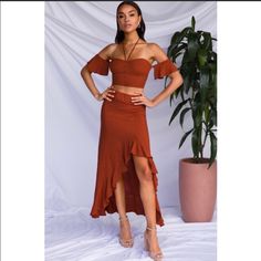 a woman standing in front of a potted plant wearing a brown skirt and crop top