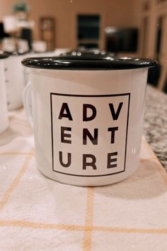 two white coffee mugs sitting on top of a table with the words adventure printed on them