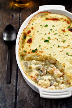 a casserole dish with meat and cheese in it next to a spoon on a wooden table