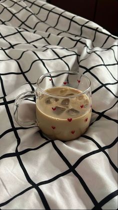 a glass mug filled with liquid sitting on top of a bed