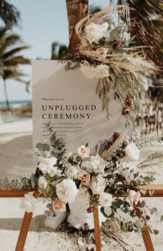 an unplugged ceremony sign with flowers and greenery on the beach in front of palm trees