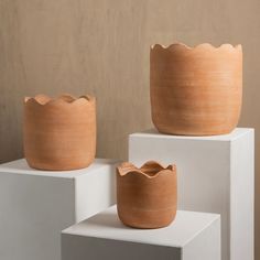 three clay pots sitting on top of white pedestals