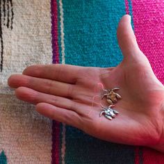 a person's hand holding several small pieces of jewelry in their palm on a colorful blanket