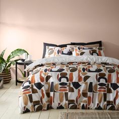 a bed with an orange and black comforter on it in a bedroom next to a plant