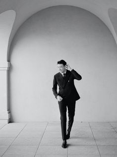 a man in a suit and tie talking on a cell phone while standing against a wall